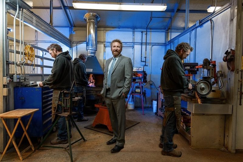 Travis Burns (at center) wearing a suit while other versions of Travis Burns (at left and right) are doing farrier work in the Farrier Shed at the Virginia-Maryland College of Veterinary Medicine. 