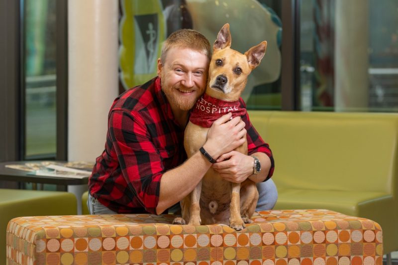Rex Williams (at right) and his owner Ross Williams (at left) hugging and posing for a photo in the lobby of the Veterinary Teaching Hospital